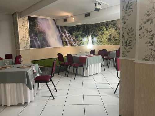 Comedor del Hotel JM El Emigrante con sillas burdeos, manteles blancos y murales de naturaleza en Villanueva de la Serena