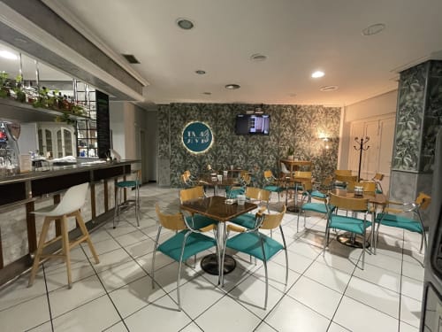 Área de café del Hotel JM El Emigrante con sillas turquesas, mesas de madera y papel tapiz estampado en Villanueva de la