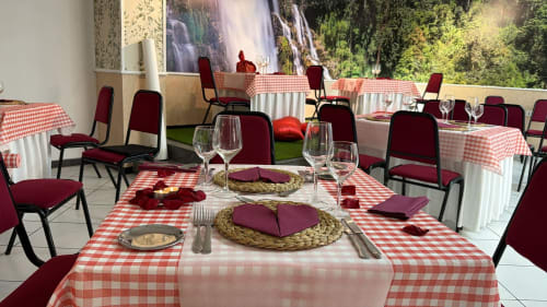 Comedor del Hotel JM El Emigrante con mesas de cuadros rojos, cubiertos, copas de vino y sillas burgundy con vista al