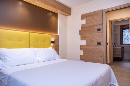 Camera moderna presso Enro Mountain Vacation Home a Roccaraso con testata gialla, dettagli in legno e bagno en-suite