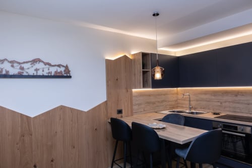 Cucina moderna nella Casa Vacanze Enro Mountain di Roccaraso con bancone in legno, sgabelli neri e luci soffuse al soffitto