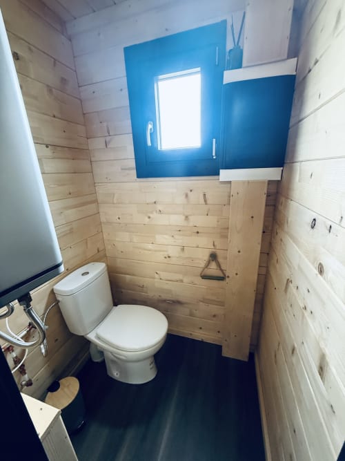 Salle de bain compacte de la villa Lodge Shiloh avec toilettes blanches, murs en bois, mur accentué bleu et fenêtre