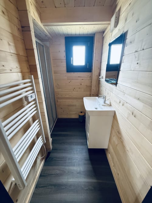 Salle de bain moderne du Lodge Shiloh aux Cabanes et lodges du Belvédère avec murs en bois, lavabo blanc, porte-serviettes et fenêtres bleues
