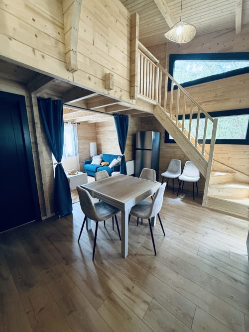 Intérieur de lodge en bois moderne avec table à manger, sièges, mezzanine et accents bleus aux Cabanes et lodges du Belvédère
