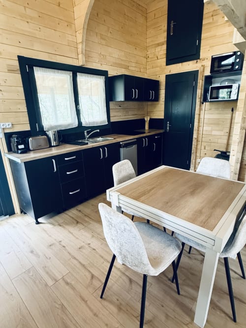 Cuisine et salle à manger de lodge moderne avec cuisines noires, murs en bois et sièges à table aux Cabanes et lodges du Belvédère