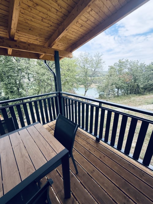 Terrasse en bois avec balustrade noire surplombant la rivière Ain aux Cabanes et lodges du Belvédère, Serrières-sur-Ain