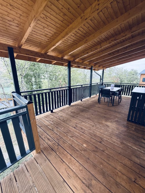 Terrasse couverte en bois avec balustrades noires dominant le lac aux Cabanes et lodges du Belvédère, Serrières-sur-Ain