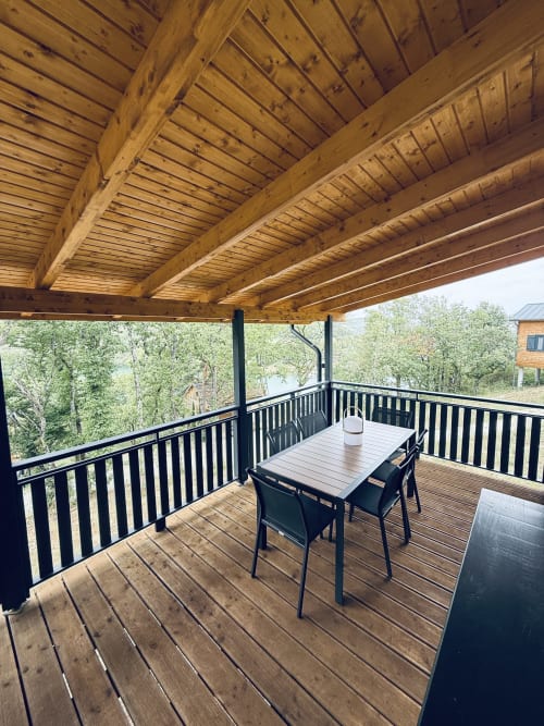 Spacieuse terrasse en bois avec table à manger sous pergola en bois, balustrade noire, vue sur forêt et lac à la villa Lodge Shiloh