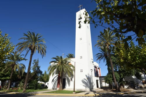 Torre blanca de iglesia con cruz rodeada de palmeras en Cal Xot B&B, Poble Nou del Delta, España