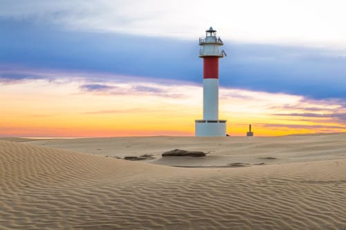 Faro rojo y blanco al atardecer en playa arenosa cerca de Cal Xot en Poble Nou del Delta, España