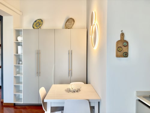 Moderna sala da pranzo nell'appartamento di Parma con mobili bianchi, tavolo in legno e piatti decorativi alle pareti
