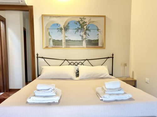 Camera luminosa con asciugamani bianchi, letto in ferro battuto e vista pastorale dalla finestra presso Manu Maison a Parma