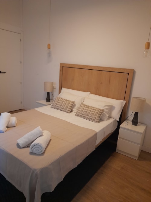 Modern bedroom at G&H Apartments in Jerez de la Frontera with wooden headboard, white bedding, and rolled towels
