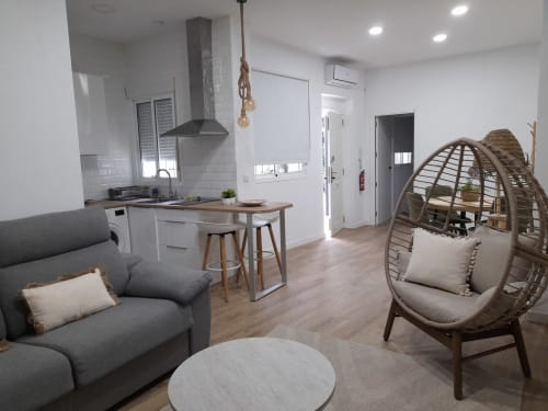 Modern open-plan apartment living area with gray sofa, woven hanging chair, white kitchen, and wooden flooring at G&H