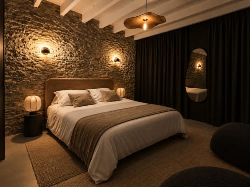 Chambre moderne aux Nuits d'audace Alès avec mur en pierre apparente, éclairage ambiant et mobilier contemporain