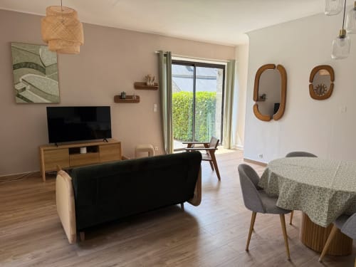 Salon de cottage moderne au Clos de l'Arguenon avec canapé noir, meuble TV en bois, coin repas et vue sur le jardin