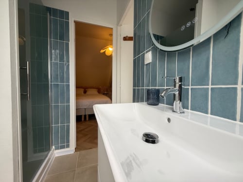 Salle de bain moderne du gîte Le Clos de l'Arguenon à Val-d'Arguenon avec carrelage turquoise, lavabo blanc et douche