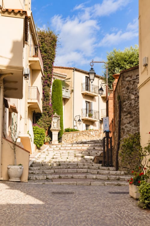 Charming cobblestone alley in Cannes with cream buildings, ivy-covered walls, and stone staircase