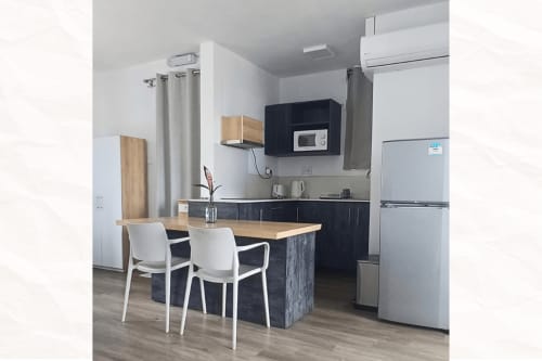 Modern kitchen with black cabinetry, wooden countertop, white chairs, and stainless steel appliances at Joubarbe Résidence,