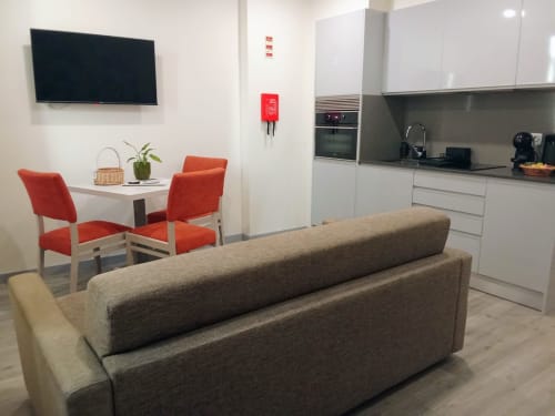Modern apartment living space at Tropical Solutions Funchal with gray sofa, red chairs, kitchen, and wall-mounted TV