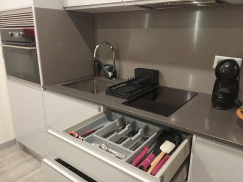 Modern kitchen with gray countertop, sink, faucet, dish rack, and open drawer with utensils at Tropical Solutions apartment
