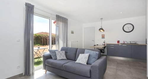 Modern open-plan living area with gray sofa, kitchen, and terrace access at Résidence des Sables, Mably