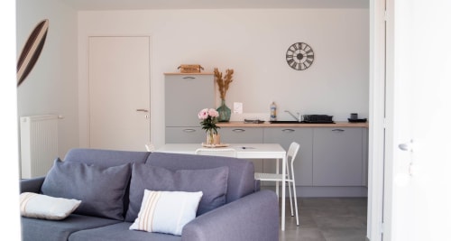 Modern Sydney apartment at Résidence des Sables in Mably with gray sofa, white dining table, kitchen, and clock