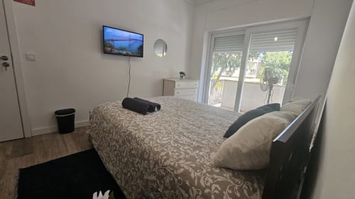 Quarto moderno no hostel Grupo Lisboa Alojamentos em Amadora com cama, TV de ecrã plano, vista de varanda e casa de banho partilhada