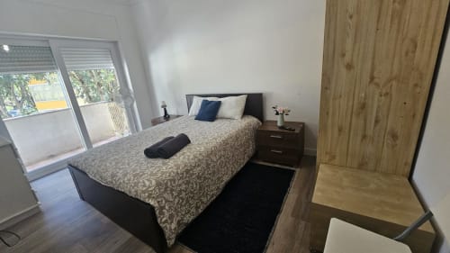 Quarto moderno no hostel Grupo Lisboa Alojamentos em Lisboa com vista para a cidade, cama de casal, criado-mudo e guarda-roupa de madeira