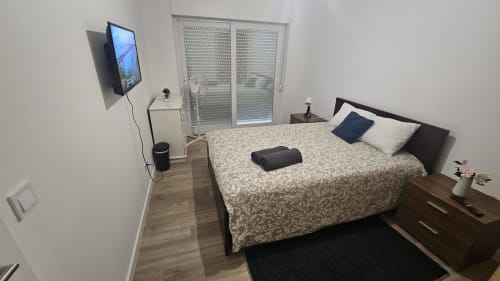 Quarto moderno na Amadora 3 Guest House em Lisboa com cama de casal, TV na parede, piso em madeira e portas com vista para a cidade