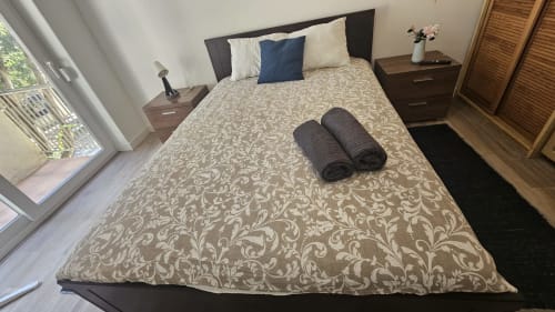 Quarto moderno no Grupo Lisboa Alojamentos em Lisboa com colcha estampada, cabeceira escura, mesas de cabeceira e vista da cidade