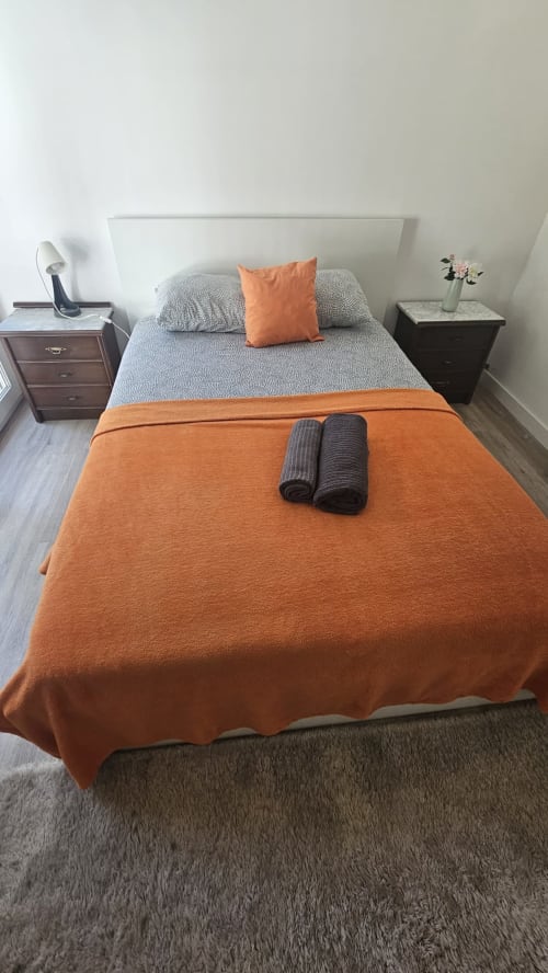 Quarto moderno na Grupo Lisboa com roupa de cama laranja e cinzenta, mesas de cabeceira e vista para a cidade em Amadora, Lisboa