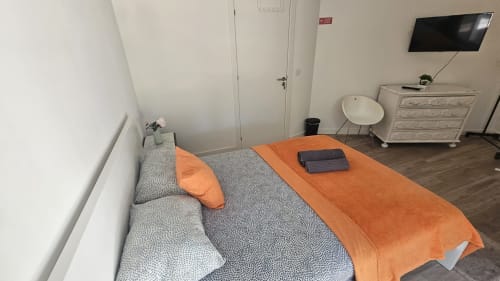 Quarto de hostel em Lisboa com cama de solteiro, manta laranja, cabeceira cinza, TV, cômoda e acesso a banheiro compartilhado