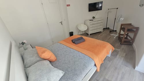Quarto luminoso na pousada Grupo Lisboa Alojamentos em Amadora com camas geminadas, roupa de cama laranja, pisos em madeira e vistas para a cidade