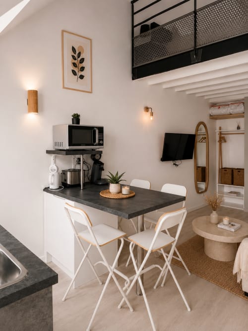 Kitchenette moderne avec plan de travail foncé, bar blanc, micro-ondes et coin repas à La Maison végétale