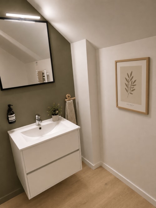Salle de bain moderne du Cocon végétal au Mans avec vasque blanche, murs vert olive et œuvres botaniques
