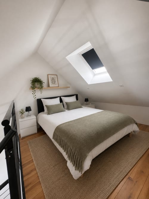 Chambre mansardée moderne au Cocon végétal au Mans avec verrière, lit à structure noire, literie neutre, parquet et plantes en pot