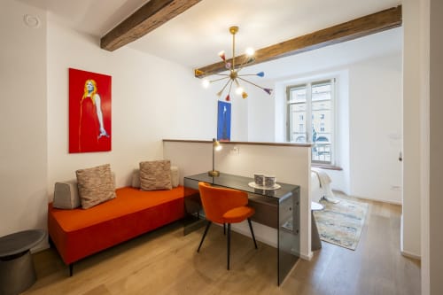 Moderna camera d'hotel a Parma con divano rosso, scrivania, lampadario dorato e travi di legno a vista