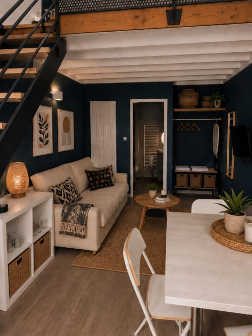 Studio moderne à La Parenthèse Mancelle au Mans : murs bleu marine, canapé crème, poutres en bois et espace ouvert