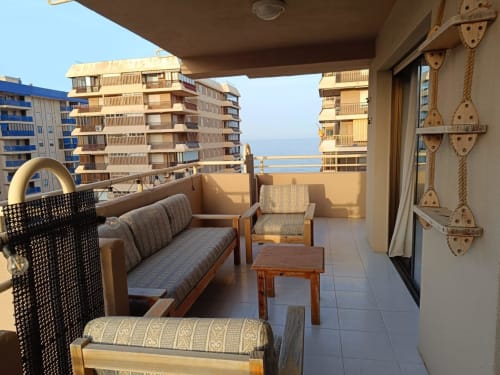 Sunny beachfront apartment terrace in Benicàssim with sea views, furnished seating, and coastal high-rises