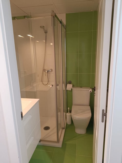 Modern bathroom at Mediterranea Sunny Keys with green tile floor, glass shower enclosure, white toilet, and vanity sink