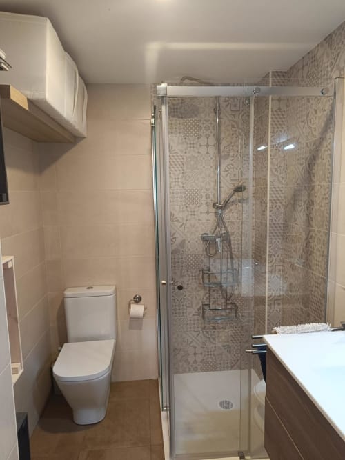 Modern bathroom with glass shower enclosure, white toilet, and patterned tile walls at Mediterranea Sunny Keys in Benicàssim