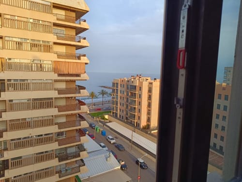 Benicàssim apartment balcony view overlooking Mediterranean Sea, beach, palm trees, and coastal buildings at sunset