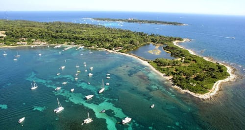 Aerial view of Cannes coastal area with anchored sailboats, turquoise waters, and lush Mediterranean vegetation