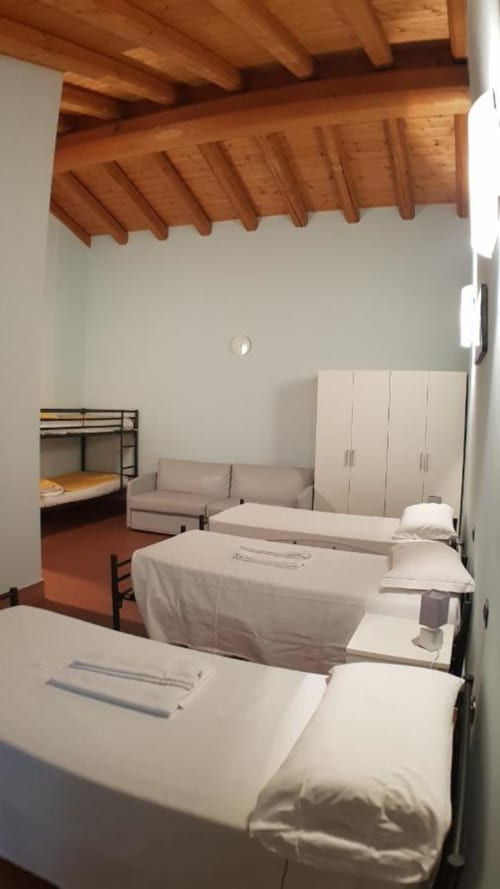 Schlafsaal im Ostello Molino di Basso mit mehreren Betten, Holzbalkendecke und Kleiderschrank