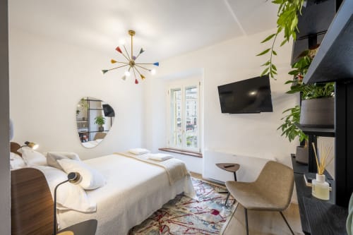 Camera moderna dell'hotel a Parma con letto, TV a parete, plafoniera colorata, specchio, piante verdi e vista sulla città