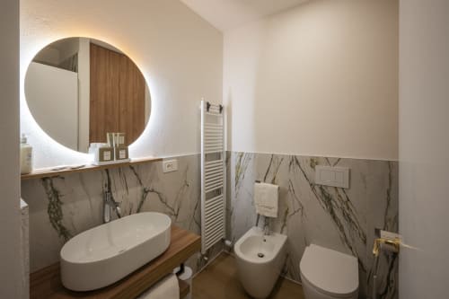 Bagno moderno di Manu Maison a Parma con specchio illuminato rotondo, rivestimenti in marmo, lavabo bianco ovale, bidet e scaldasalviette