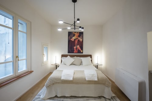 Camera da letto moderna e luminosa a Manu Maison a Parma con letto in legno, biancheria bianca, luci sospese e ampie finestre