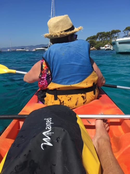 Two kayakers paddling in turquoise Mediterranean waters near Cannes with sailboats and coastline in background