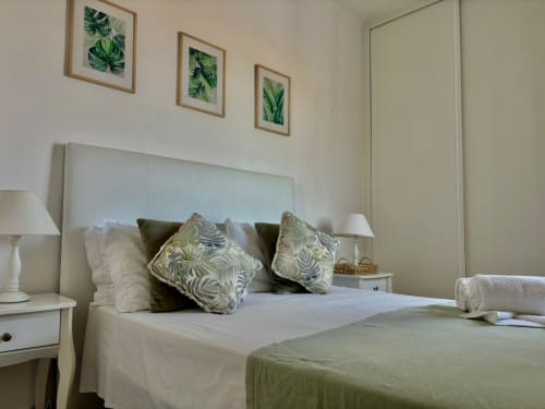 Quarto moderno do hotel Al Mare Ocean View em Albufeira com arte botânica verde, roupa de cama branca e vista para a cidade
